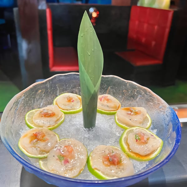 Agami Sushi's scallop sashimi on lime slices, served on ice in a blue glass bowl.