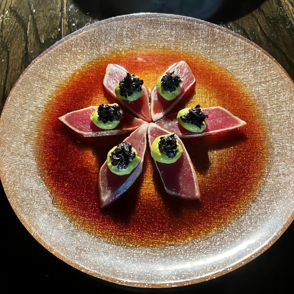 Seared tuna sashimi slices arranged in a flower shape, topped with avocado puree and black caviar.