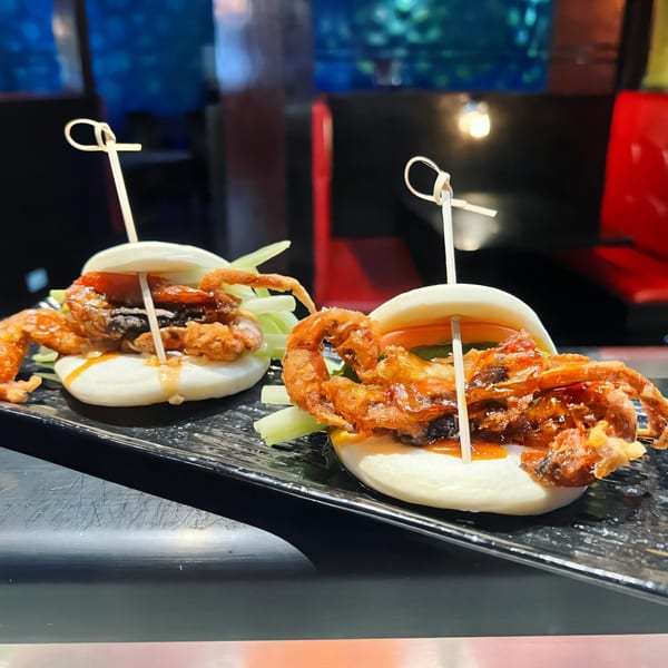 Two Agami Sushi soft shell crab bao buns with sauce and lettuce on a black plate.