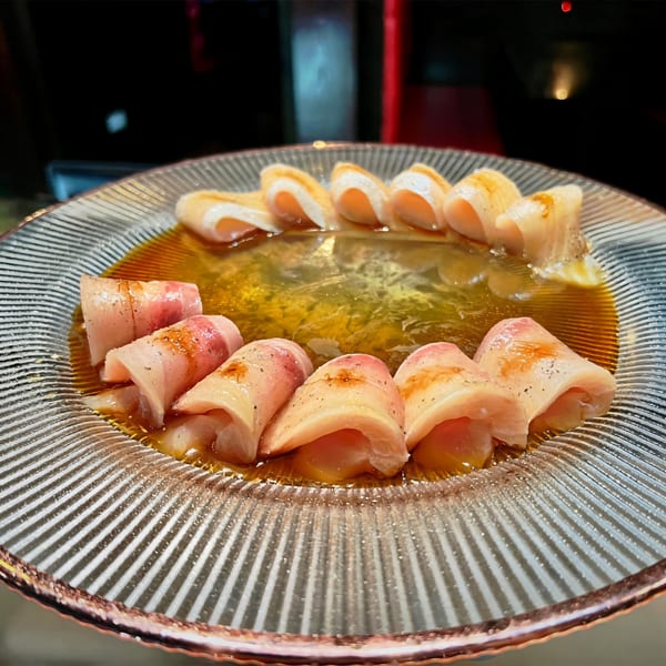Agami Sushi's delicate white fish sashimi, drizzled with sauce, arranged on a clear glass plate.