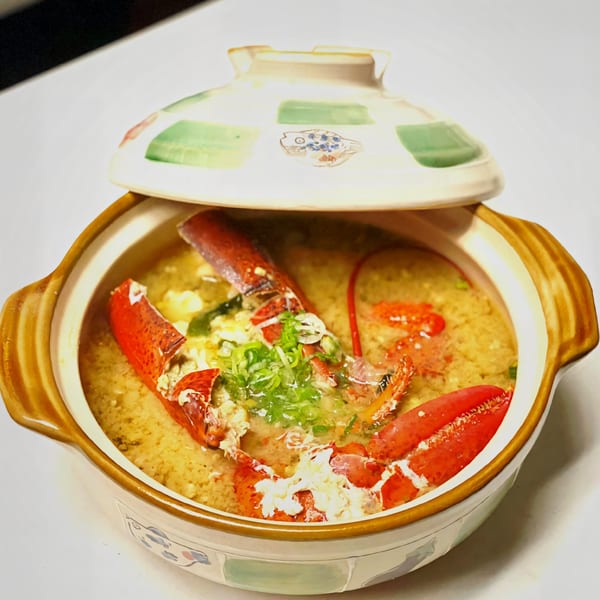 A ceramic pot of Agami Sushi's lobster miso soup, garnished with green onions and a partially open lid.