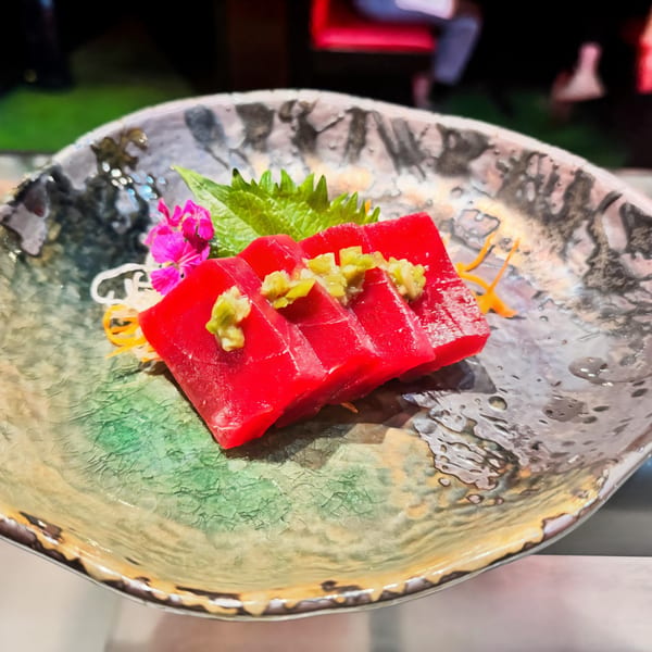 Agami Sushi's tuna sashimi, topped with wasabi, on a decorative plate with green and orange garnishes.