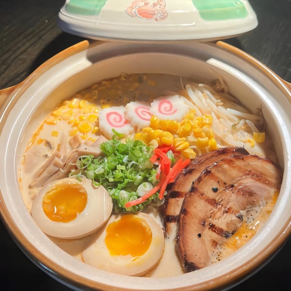 Creamy ramen in a bowl with pork, soft-boiled eggs, corn, scallions, and fish cakes.